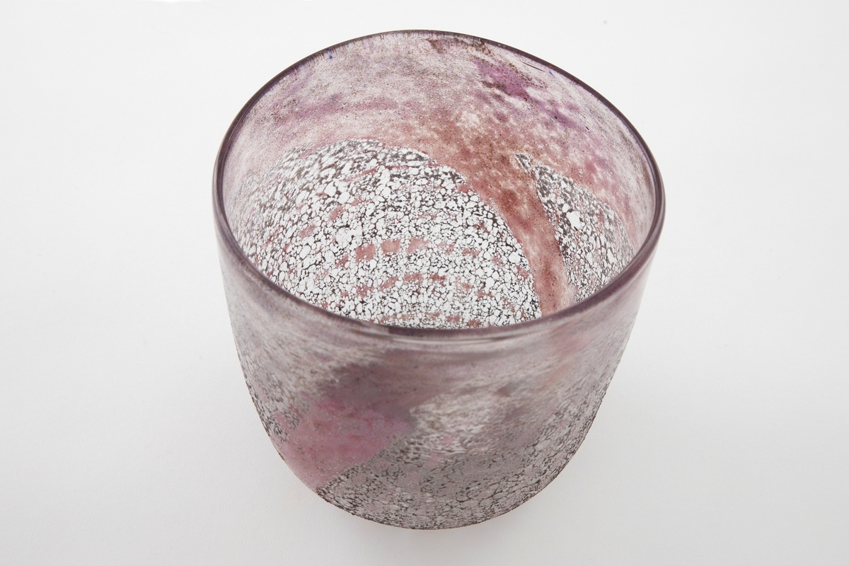 Tilnærmest halvkuleformet bolle i glass. Korpus er dekorert med emaljefarge i rødlilla fargetoner som kontrasteres med gråfarget glassfiber.