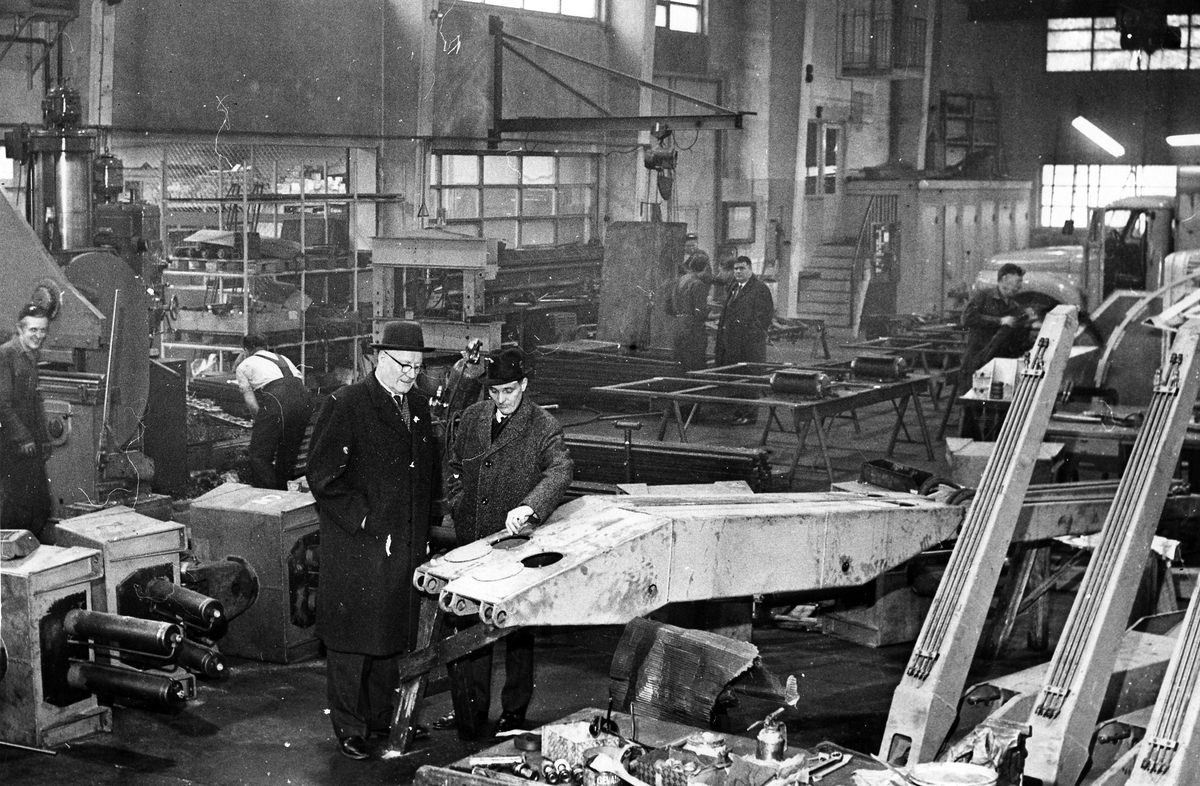 HIAB industri på Hemvägen. Två män i rock och hatt samt 4 män som arbetare vid maskinerna.