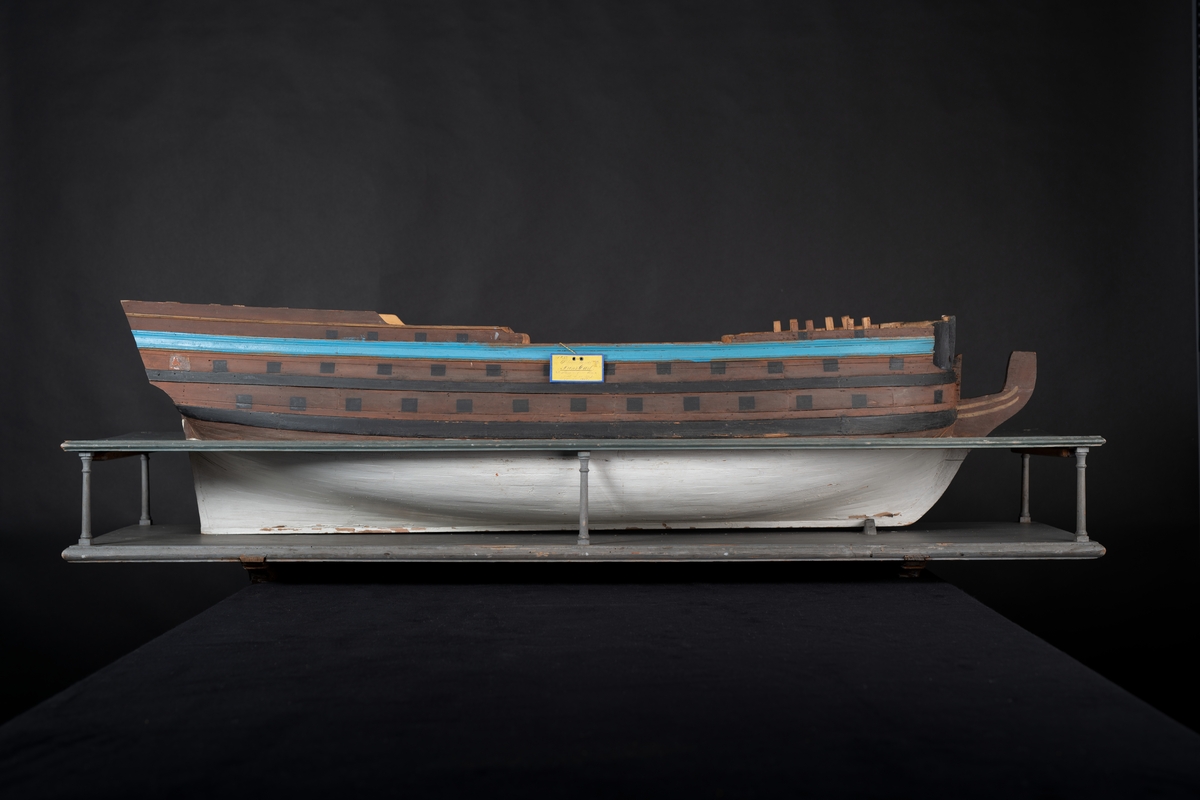 Fartygsmodell 60-kanonskeppet Prins Carl, skrovmodell. Bordläggningen limmad på gavlar, utan inredning, galjon och akterspegel. Modellen är brunmålad upptill med blå rand och svarta kanonportar. Under vattenlinjen vitmålad.