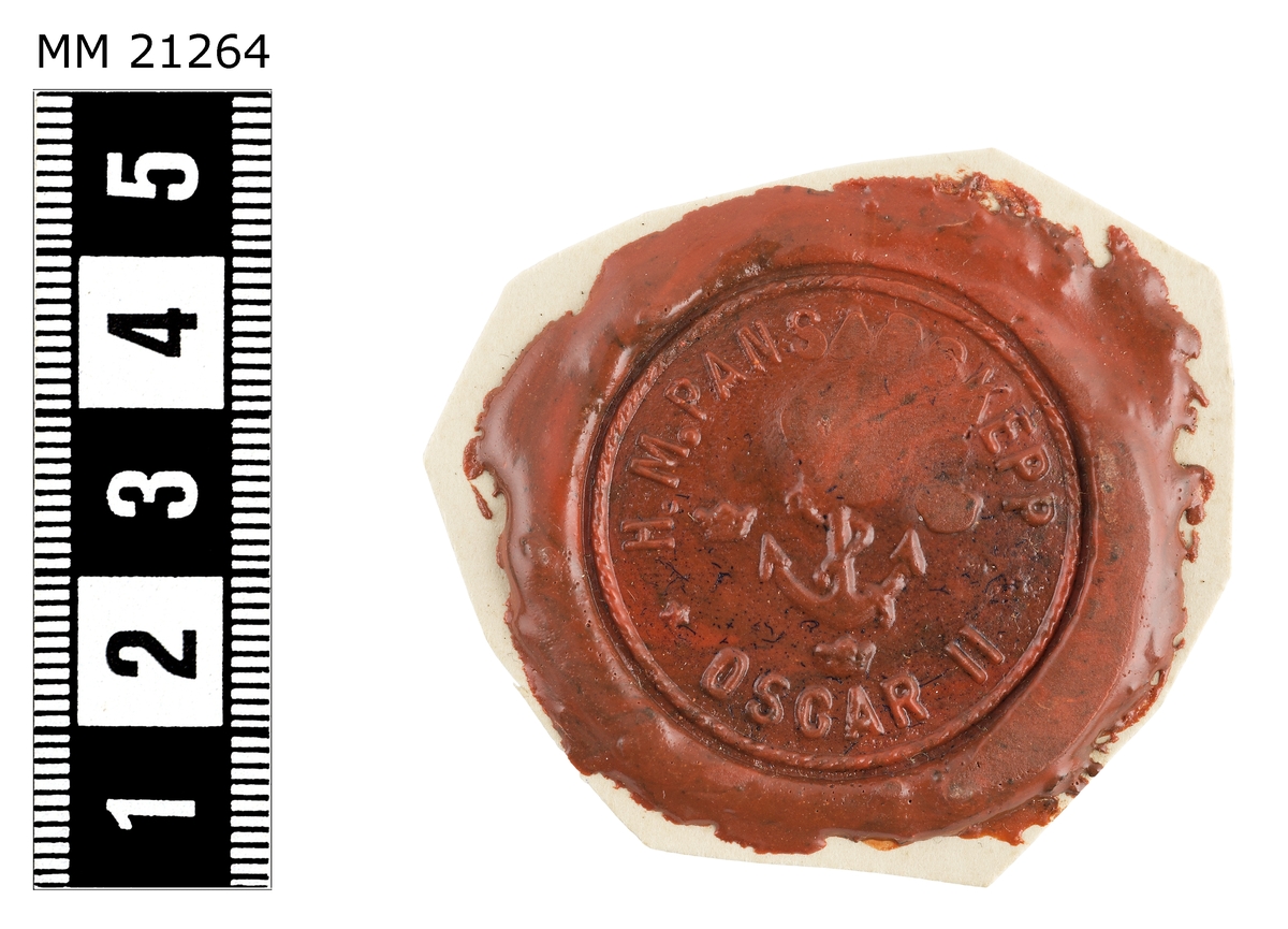Sigillavtryck av rött lack på papper. I mitten krönt stockankare omgivet av tre kronor. Längs kanten text: "HM pansarskepp Oscar II".