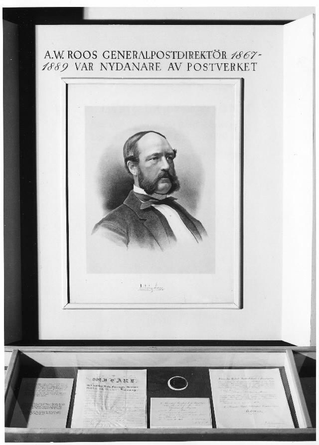 Skärmen presenterar Adolf Wilhelm Roos generalpostdirektör
1867-1889 postverkets nydanare. Porträttet är hämtat från en samtida
målning. I montern ligger handlingar med anknytning till Roos.