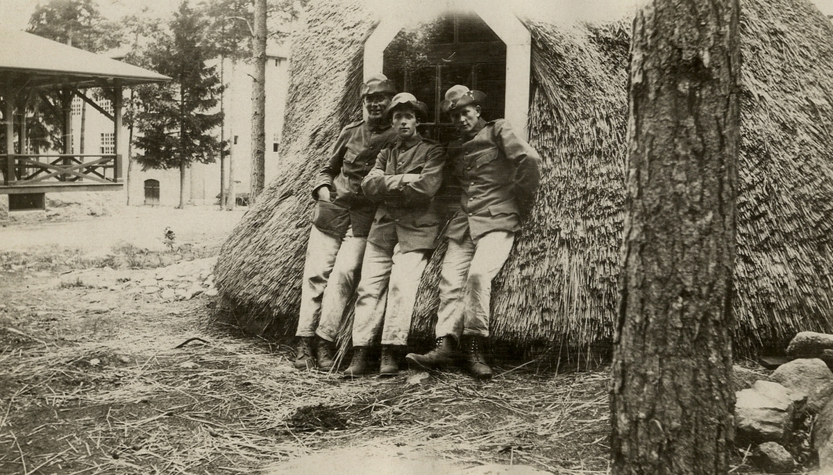 Tre meniga soldater i m/10 poserar framför en av hyddorna i regementsparken på det nya I 11.
Växjö, som skymtar i bakgrunden. Ca 1925.