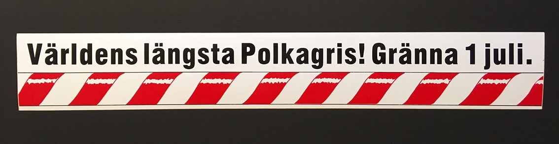 Avlång polkagrisrandig dekal med texten: "Världens längsta Polkagris! Gränna 1 juli."
