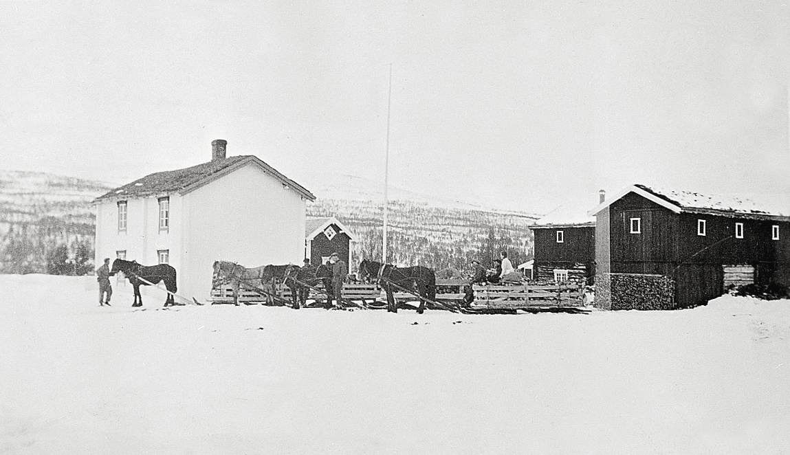 Lasskjørere og fire hester med lass foran gårdsbebyggelsen på Haugen på Sevatdalen