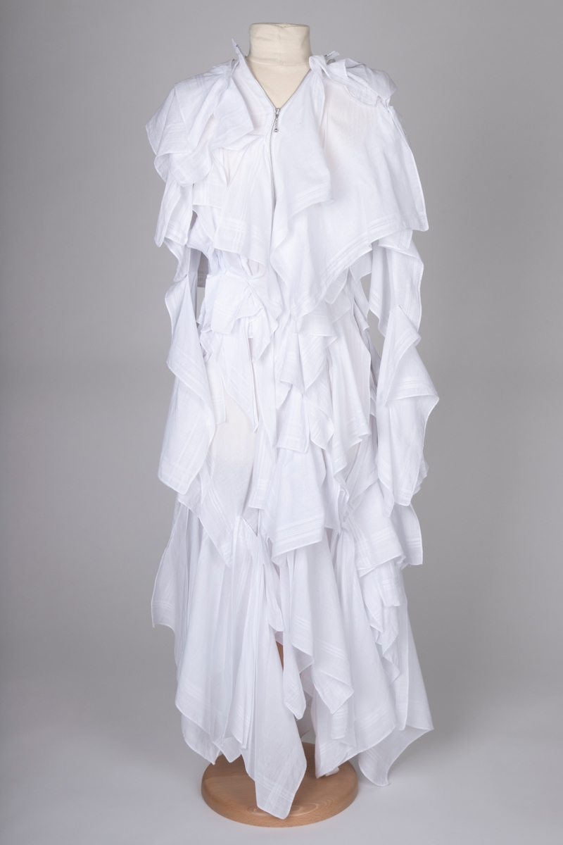 Hvitfarget kjole bestående av bomullslommetørkler, utført i "Similar Draping"-teknikk. Plagget har et sterkt dekonstruert preg, hvor man skulpturelt danderer tørklene rundt bærerens kropp.