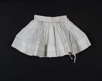 Underkjol för barn, av vitt bomullstyg, rynkat mot linningen. Nedtill två breda veck. Sprund bak, långa knytband. Tvättad i juli 1972. Inköpt i juni 1972 från Emmaus.