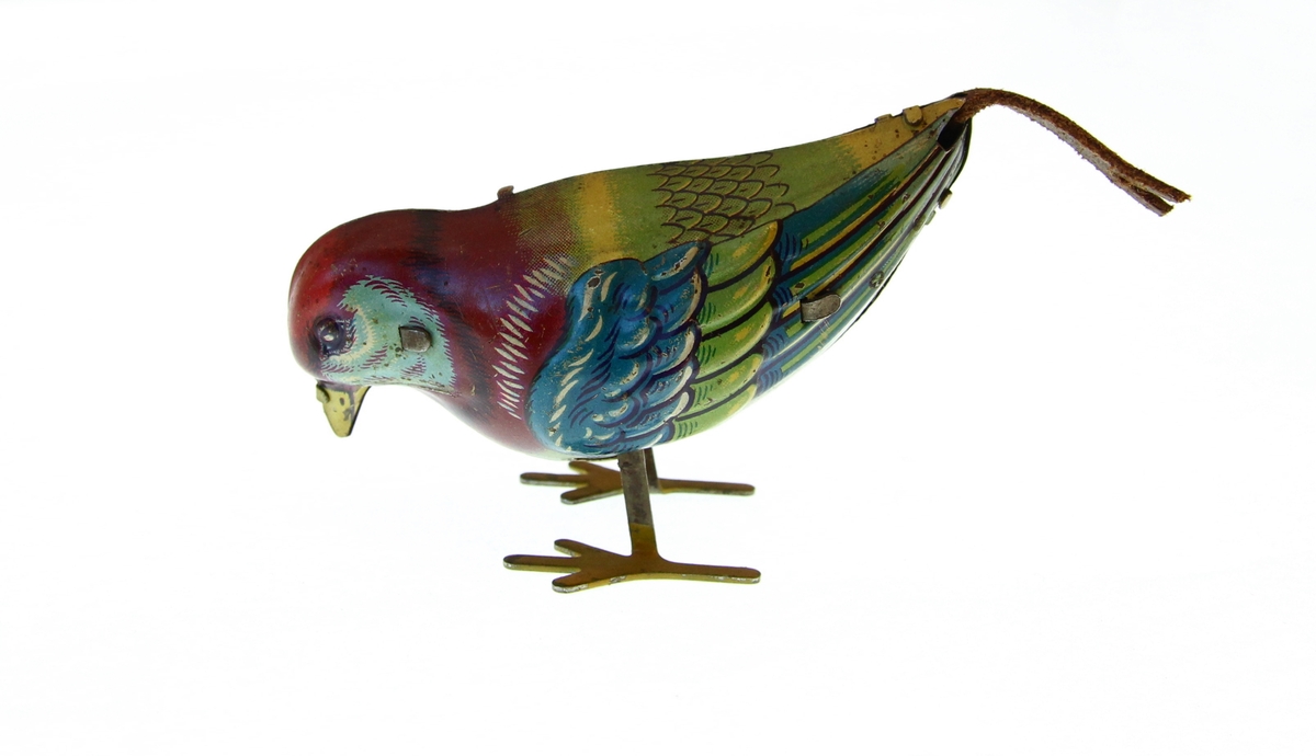 Leke: fugl av metall og opptrekknøkkel. Hopper på metallføtter. Stjert av lærreim. Rødt hode, mangefarget.