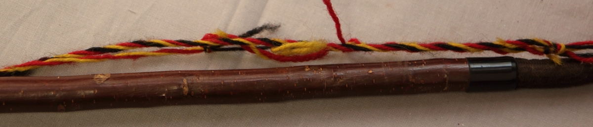 Lång pipa. Huvudet bestående av ett stycke trä med snidade detaljer. Lock av mässing. Mässing även vid huvudets övre del där det går samman med halsen/munstycket. Halsen bestående av ett stycke trä. Med ett flätat band i gul, röd och svart tråd.