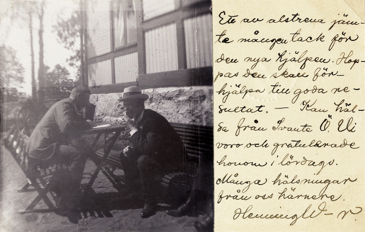 Två män i kostym och hatt sitter vid ett trädgårdsmöblemang intill ett bostadshus, 1909.
Tingsryd (?).