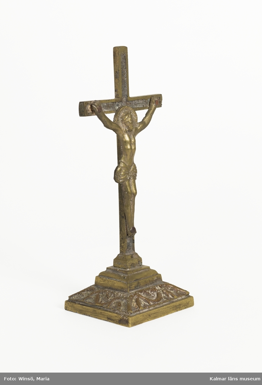 KLM 10337. Krucifix. Av brons, gjuten. På fot. Jesusfiguren är fastnitad i korset.