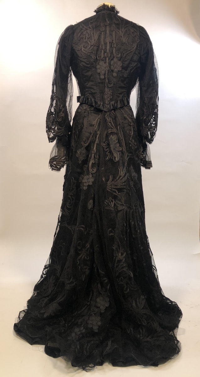 Todelt, svart kjole med skjørt og kjoleliv samt tilhørende kep. Kjolen har angivelig vært Emilie Andrea Jerstads brudekjole. 

