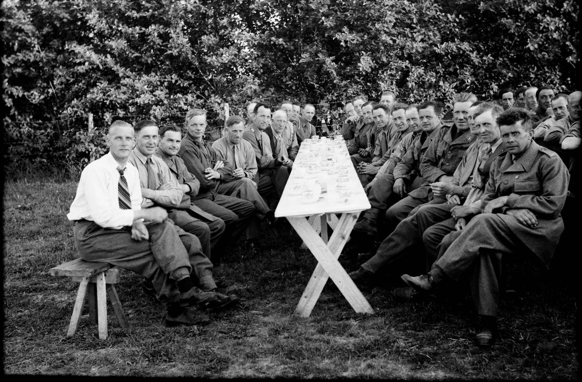 Kaffekalas vid långbord under beredskapen vid andra världskriget, sannolikt i Grimeton. Somliga bär uniform medan andra sitter i bara skjortärmarna.