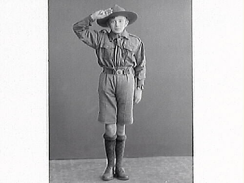 Pojkporträtt av en pojke i scoutuniform som gör scouthälsning. Fru Hellborg beställde bilderna.