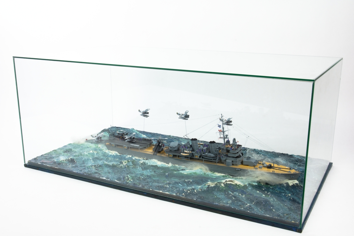 Modell av fartyg; flygplanskryssare Gotland. Sceneri monterad i glasmonter.