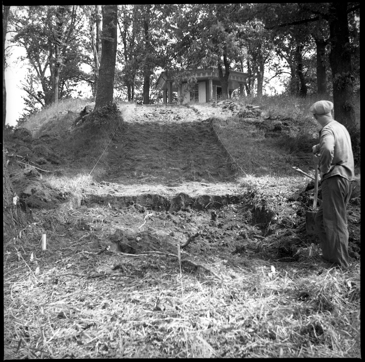 Avtorvningen av Schakt D genom södra delen av borgkullen vid Rumlaborg i Huskvarna är avklarad och fortsatta grävningar kan ta vid. På borgkullens topp skymtar lusthuset och vid sidan av står en man med spade. Bilden togs i samband med arkeologiska undersökningar vid borgen sommaren 1938.