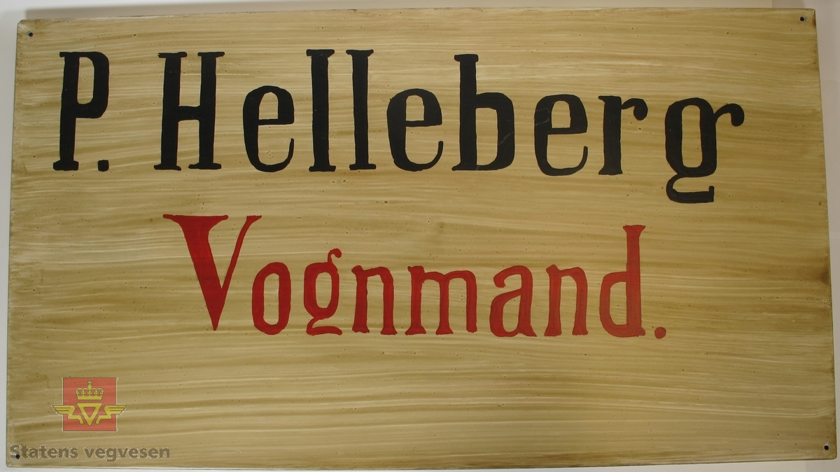 Rektangulært skilt lagd av metall, med teksten "P. Helleberg" med svarte og "Vognmand" med røde bokstaver på hvit/brun bakgrunn. Det er laget et hull i hvert av hjørnene.