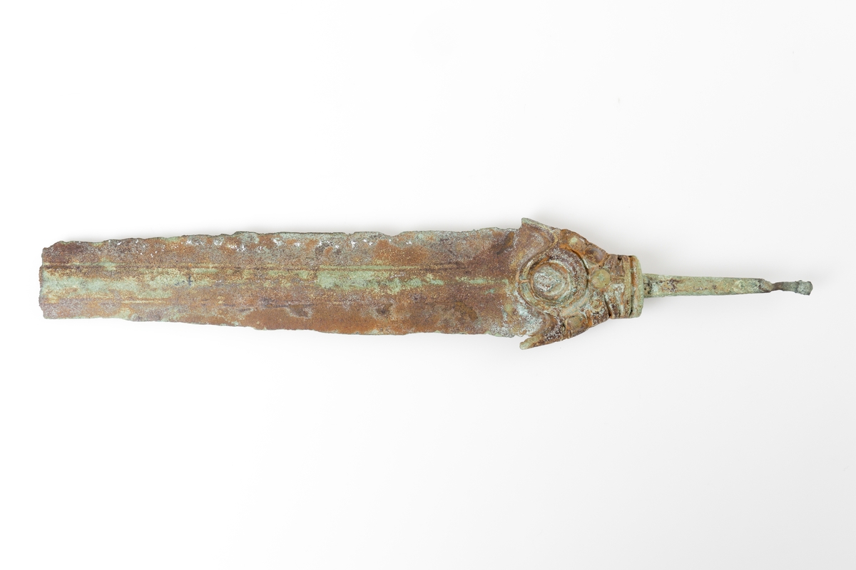 Bronsdolk eller möjligen svärd vars fäste har stora likheter med svärd nr 1001 i Montelius, O. (1917). s. 66. Helgjutet fäste som övergår i en smal tånge.