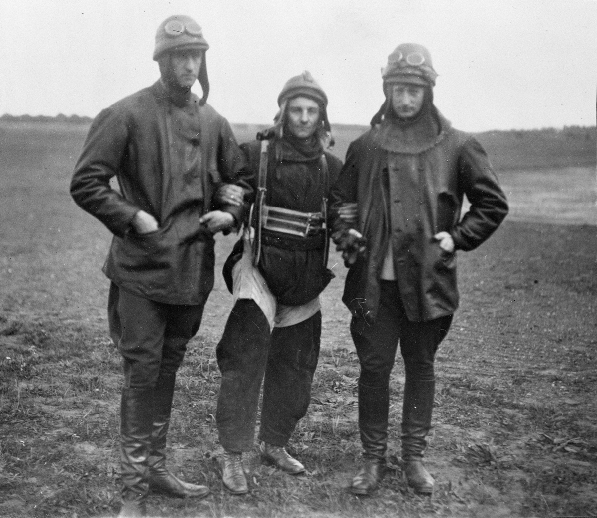 Fallskärmshoppare (i mitten) samt två militära flygare står på ett fält, 1919.