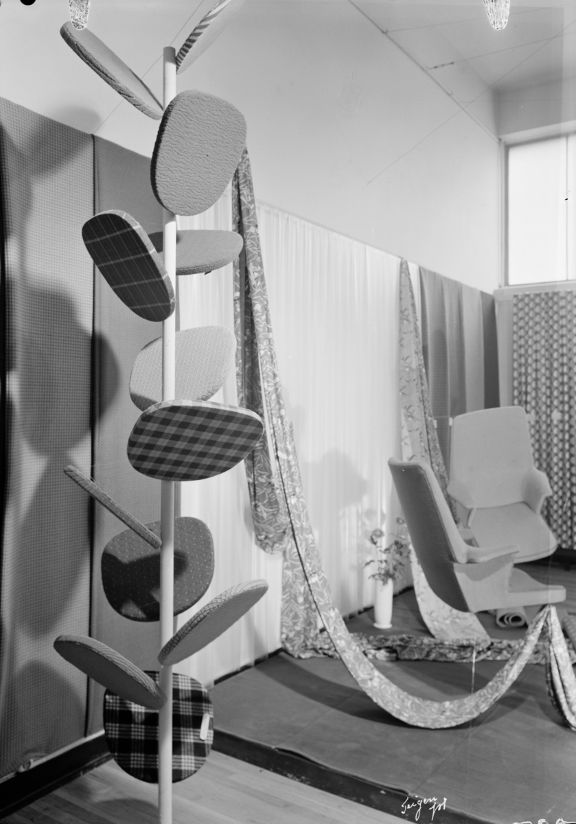 Utstillingen "Norsk tekstil 1952" med stolerseter trukket med vevde møbelstoffer, trykte og gjennomskinnelige gardiner og teppeprøver.
