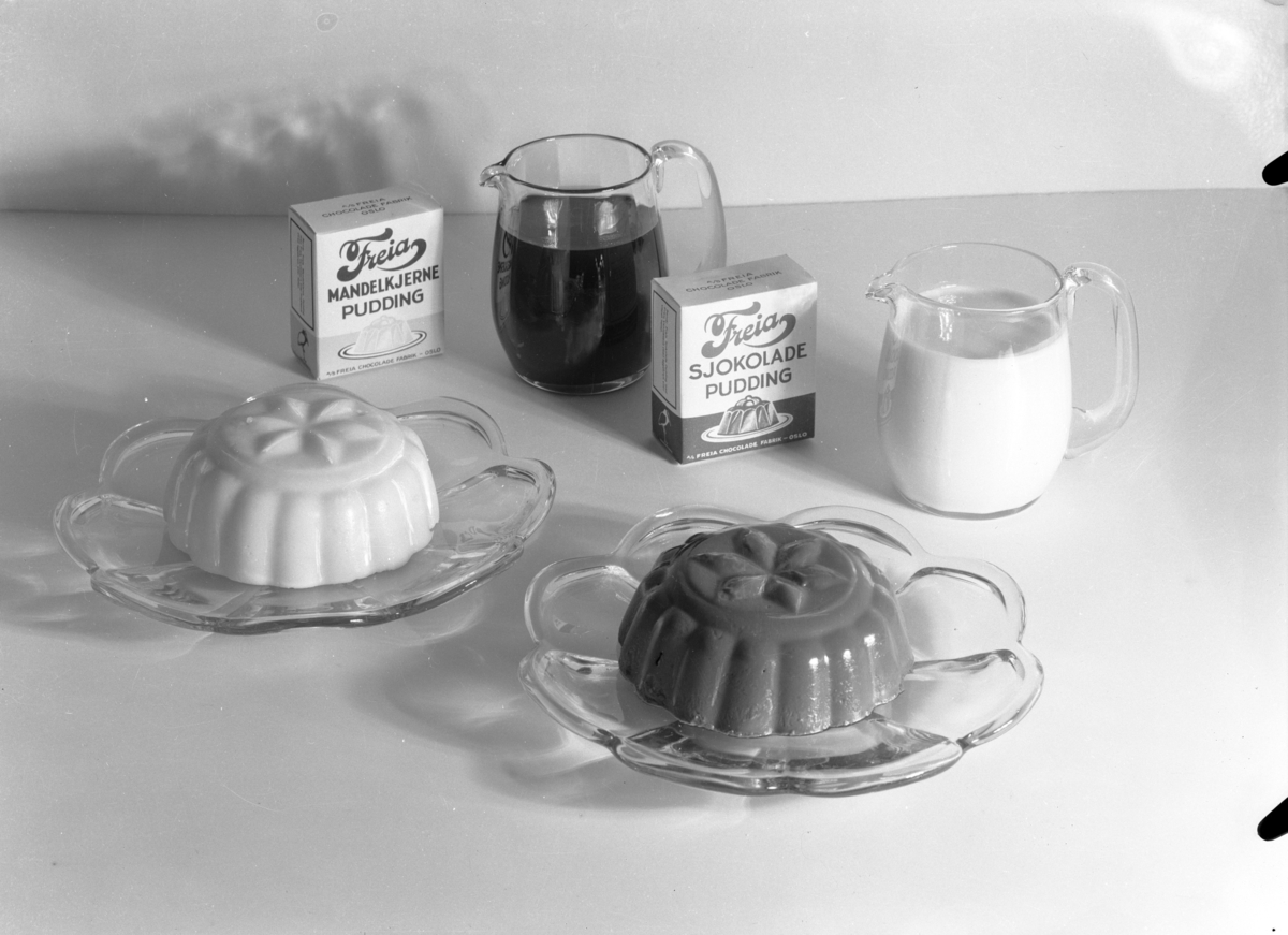 Produktfoto av esker med mandelkjernepuddingpulver og sjokoladepuddingpulver sammen med puddinger og saus.