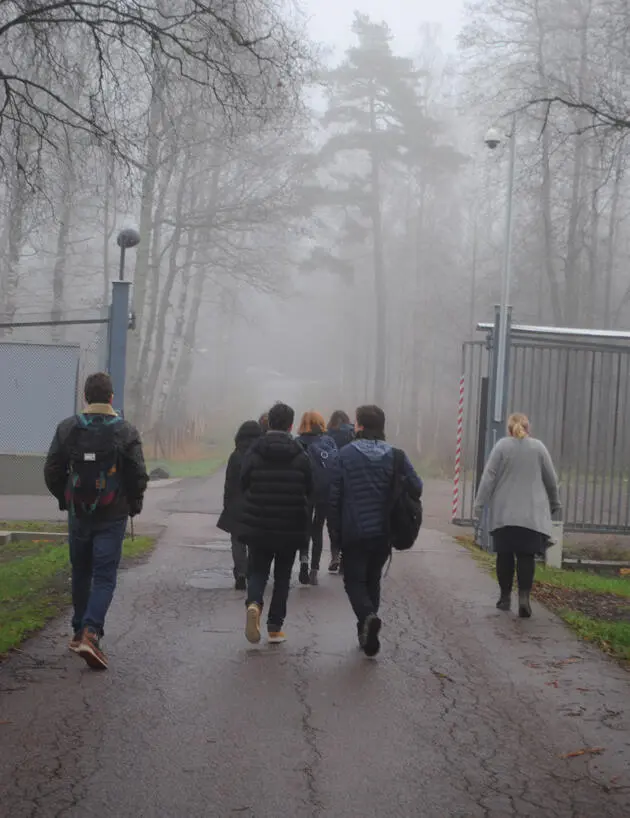 Vi ser ryggene til en gruppe mennesker til fots på vei gjennom en port i tåke