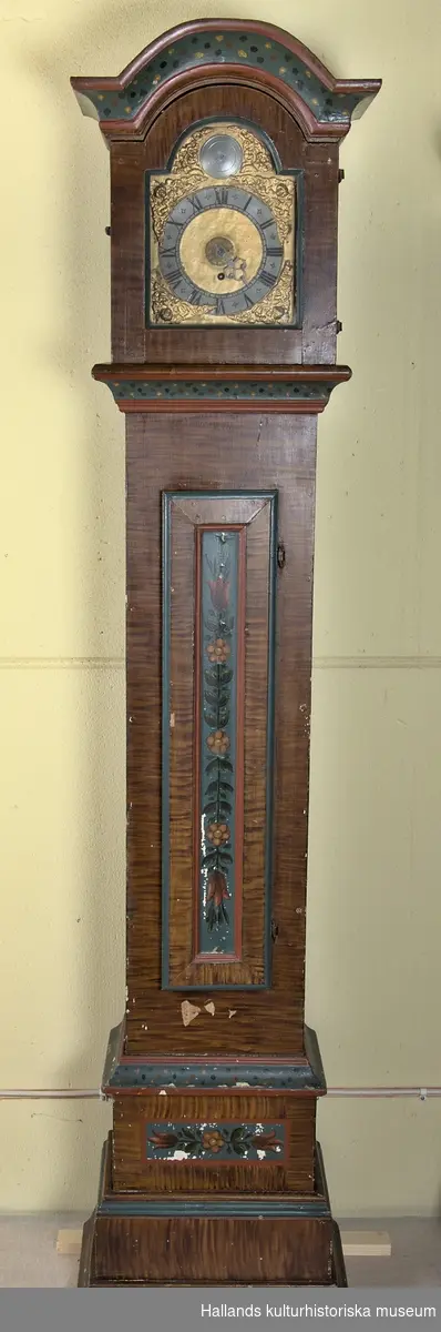 Golvur. Uret har en ådringsmålad bottenfärg i mörkbrun kulör. Dess dörr samt bottenpanel är dekormålad med färgglada blomsterrankor på turkos botten. Uret har dekorativa konsoller bemålade med gula, röda och blå prickar på turkos bottenfärg, kantade med ljusröd färg. 

Klockhuset är inramat med en glasad lucka. Urverket har en större tavla samt en mindre i dess mitt. Romerska siffror.
Stort och massivt lod av järn - se bild.

Märkt med årtalet "år 1795", samt signaturen på OAS på insidan av dörren.