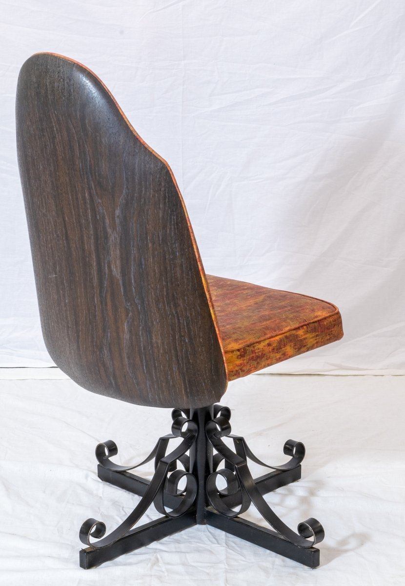 Spisestuestol med rødbrunt trekk. Bein i sort metall minner om smijern og bakplate i plast med tremønster. Stolen kan snurre.
