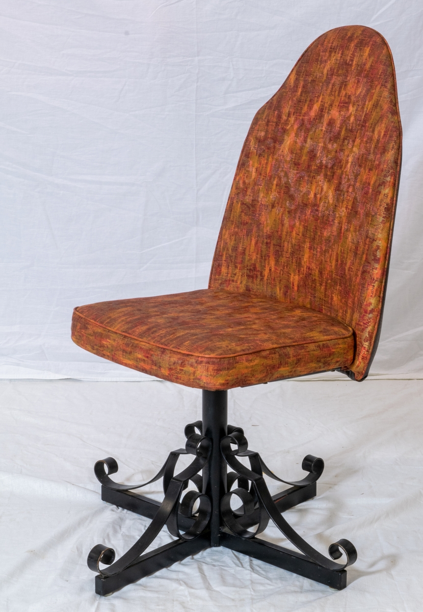 Spisestuestol med rødbrunt trekk. Bein i sort metall minner om smijern og bakplate i plast med tremønster. Stolen kan snurre.
