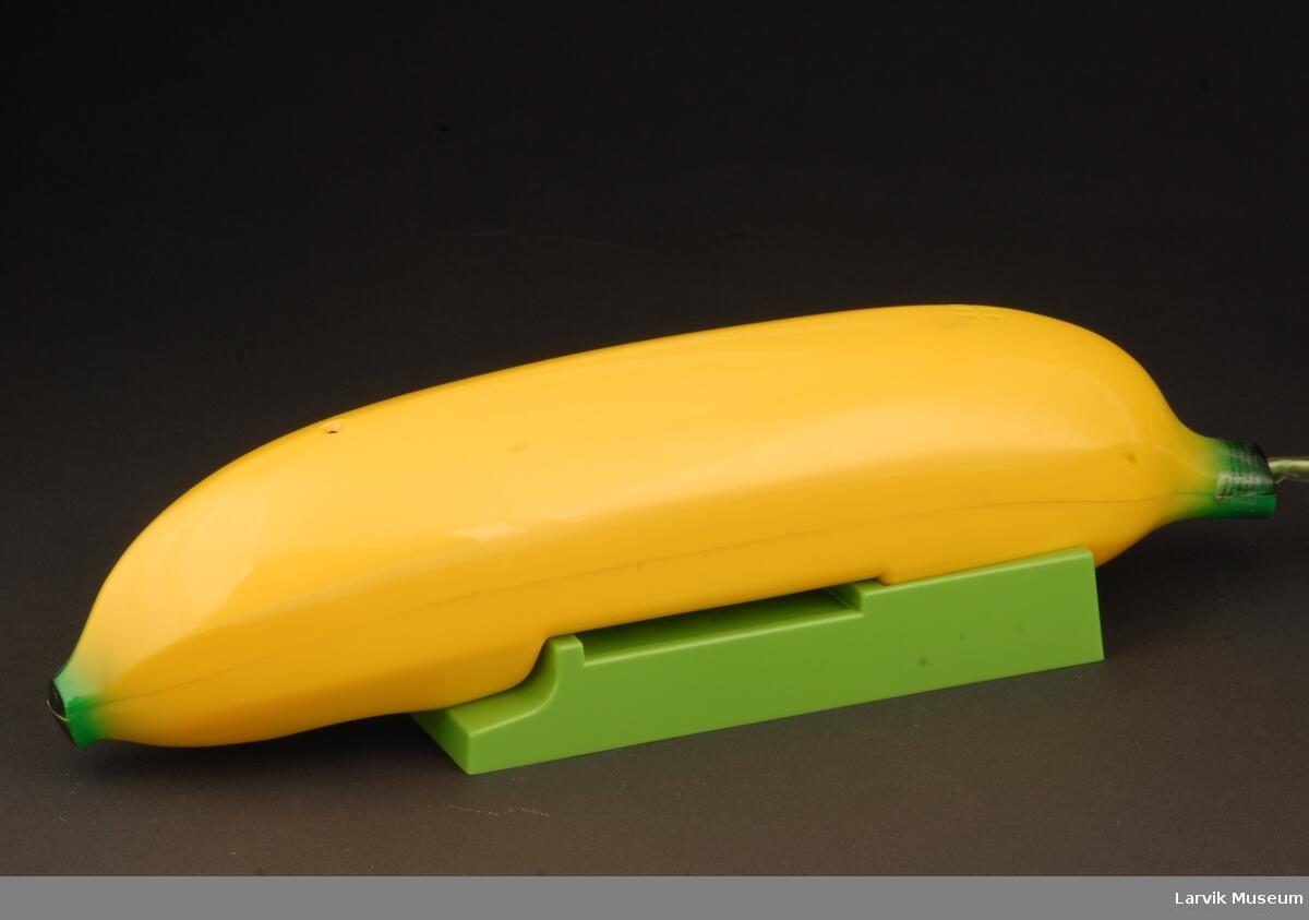 Bildet viser en gjenstand formet som en gul banan. Den ligger på en grønn plastdings.