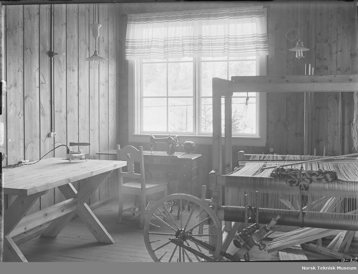 Rokk, vev, elektrisk symaskin og strykejern; stueinteriør fra mønsterbruket på NEBB's jubileumsutstilling i 1914