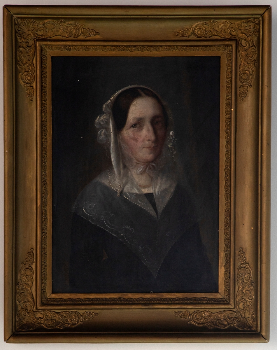 Portrett av en kvinne med mørkebrunt hår og brun-grønne øyne. Kvinnen har på seg en innendørs hodekappe i hvit med knyting i halsen og en florlett hvit krage over en svart langermet kjole. Hun bærer et perlekjede rundt halsen.