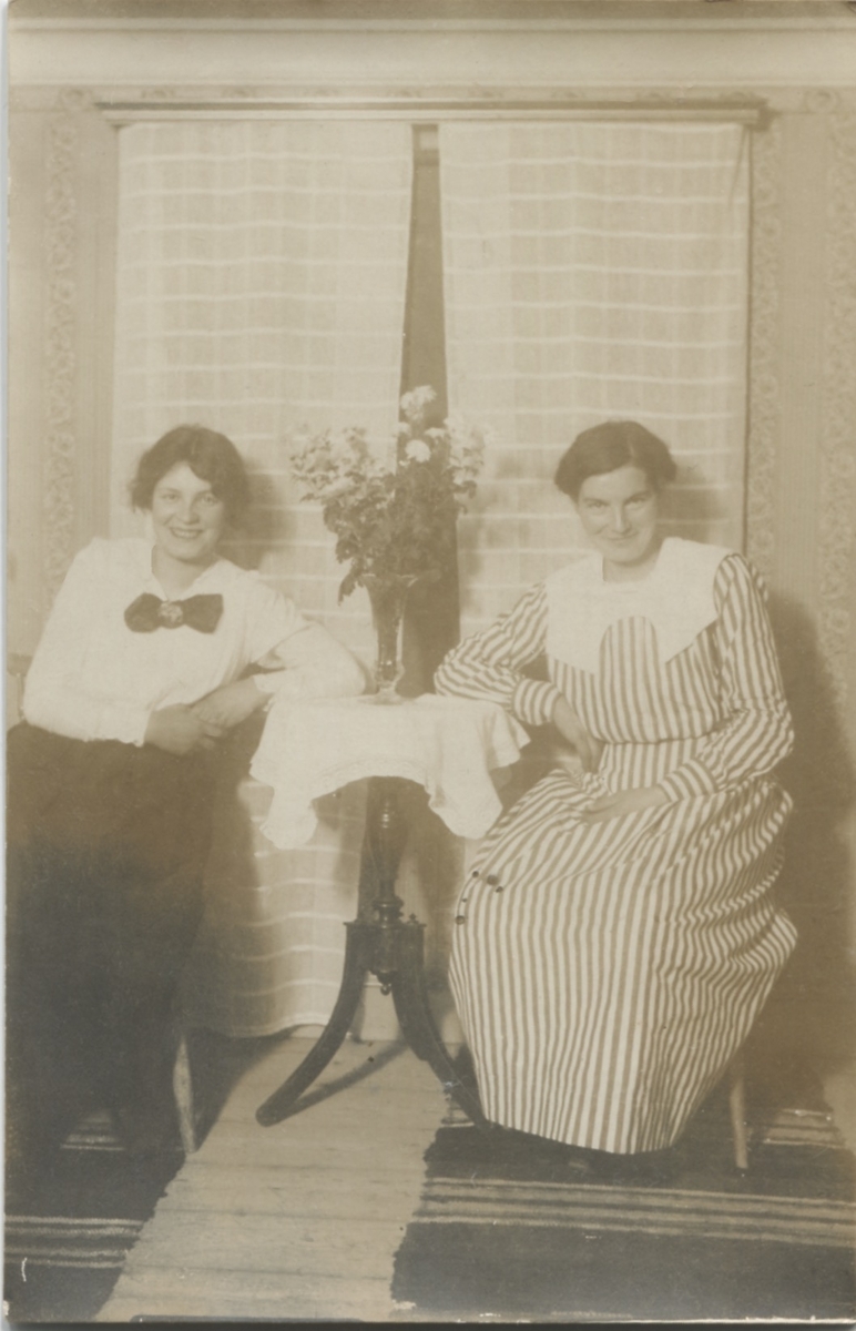 Två kvinnor sitter på var sin sida om ett litet bord framför ett fönster, okänd plats och årtal. En av kvinnorna (till höger?) är Hilda Olsson (1887-1973, 1923 gift Sandberg). Hon arbetade som husa hos Håkan Jönsson som var rektor på Stretereds skolhem. Foto från Sagered-album.