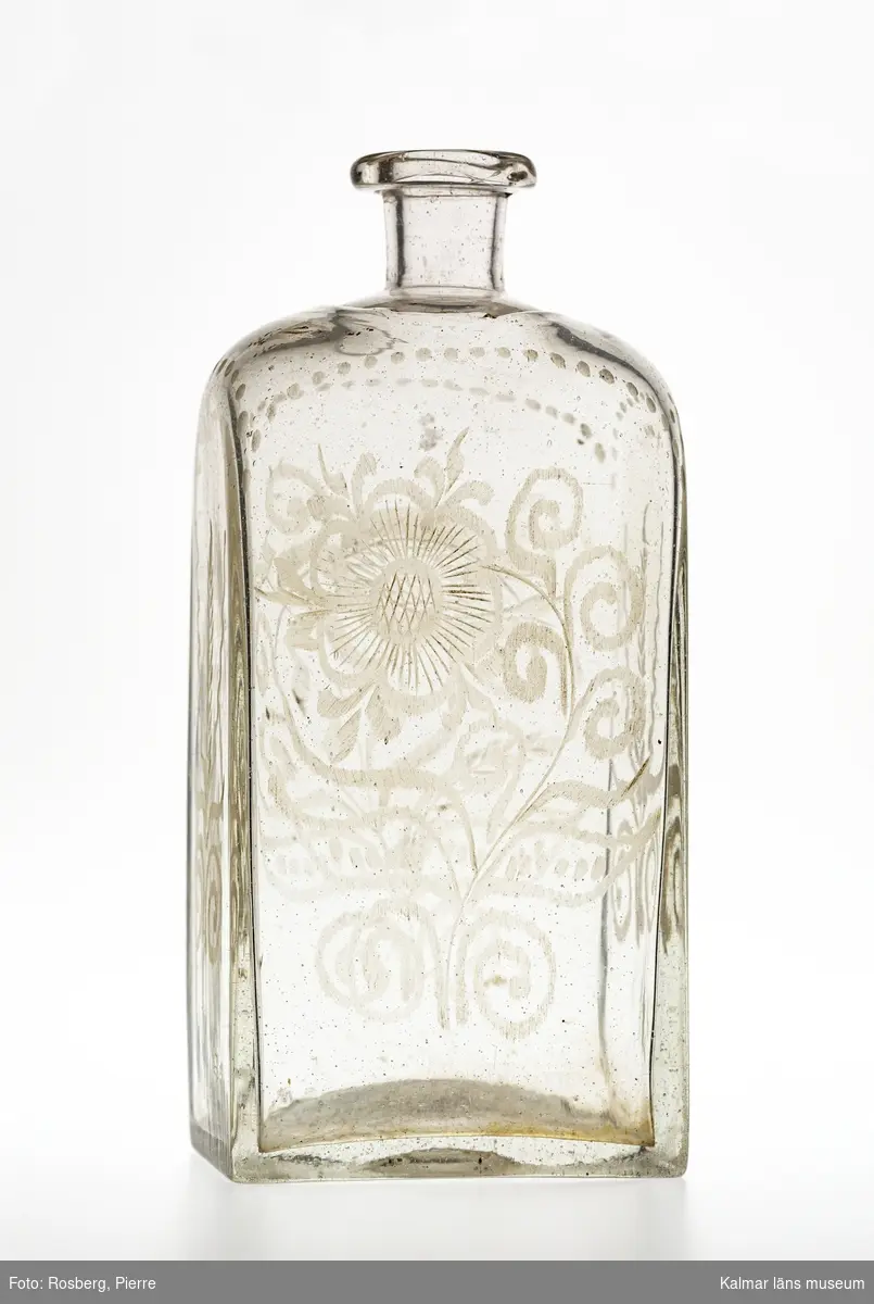 KLM 13688. Flaska, brännvinsflaska. Av glas. Fyrsidig. Graverad dekor på alla sidor i form av blommor och sädesax.