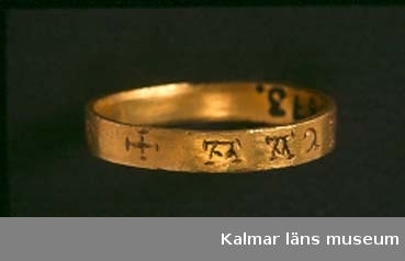 KLM 15873. Fingerring, bandformig av guld. Grekisk inskription runt hela ringen. (AMOR OMNIA VINCIT enligt B. Almgren 1948) Ska vara:  Amor vincit omnia. Förlovningsring? Datering: 1100-tal.