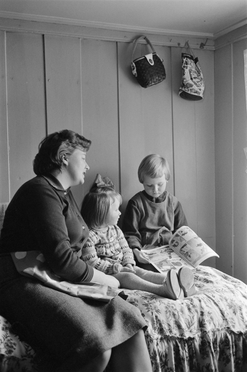 En kvinne leser et blad med to barn.