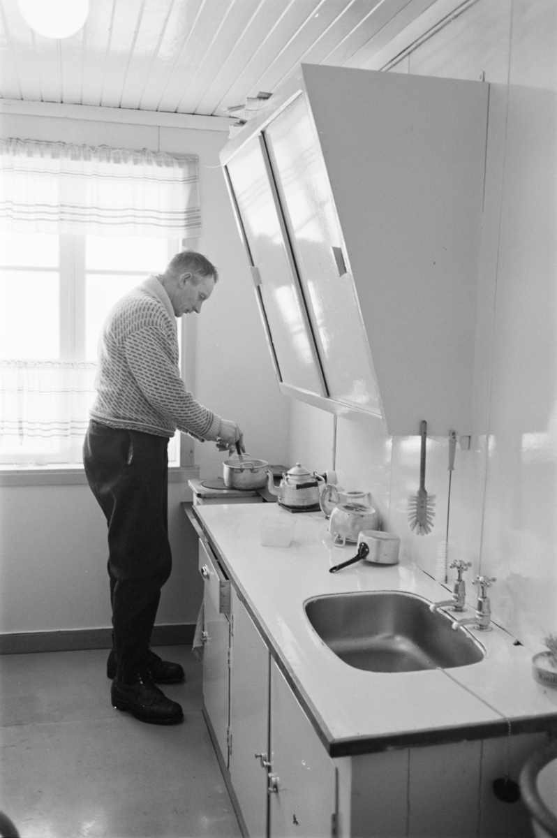 En mann rører i en gryte som står på en komfyr i et kjøkken på Røros.
