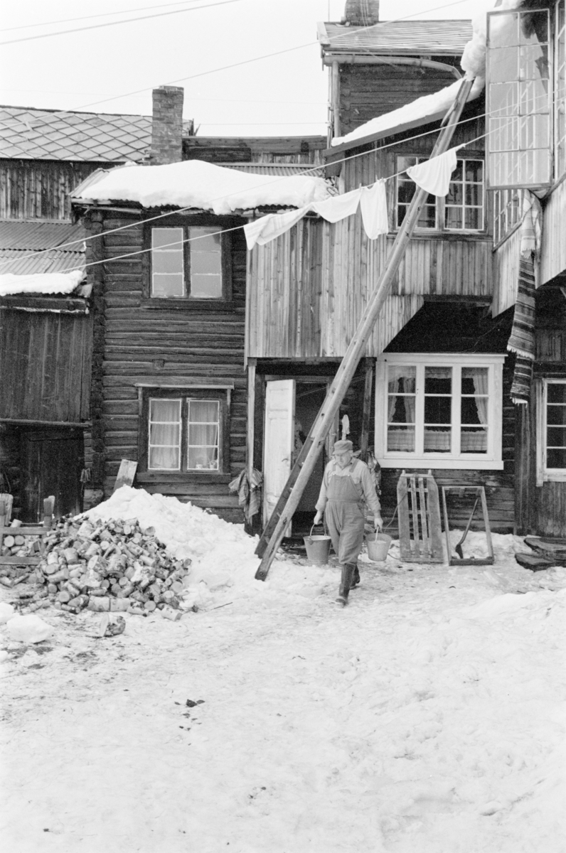 En mann med to bøtter i hendene går i snøen i et gårdsrom på Røros.