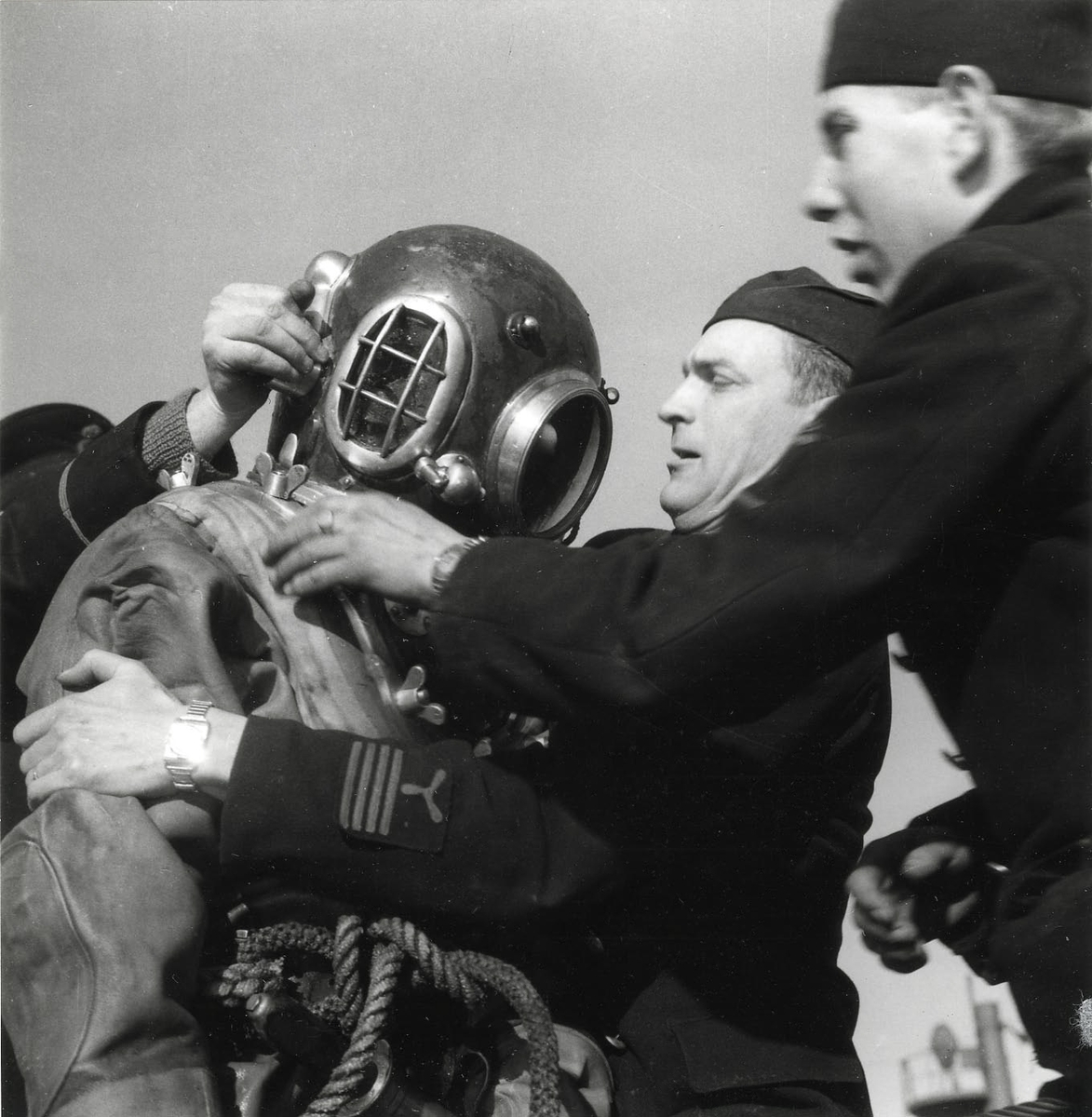 Utrustning av dykare på ubåten SJÖORMEN vid Skeppsholmen 1949. Hjälmen sättes på.