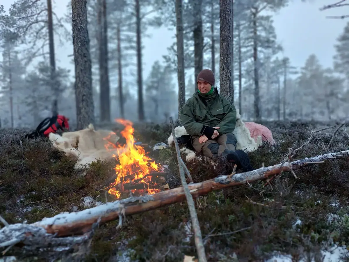 Mann sitter foran bål i skogen. Det er vinter.