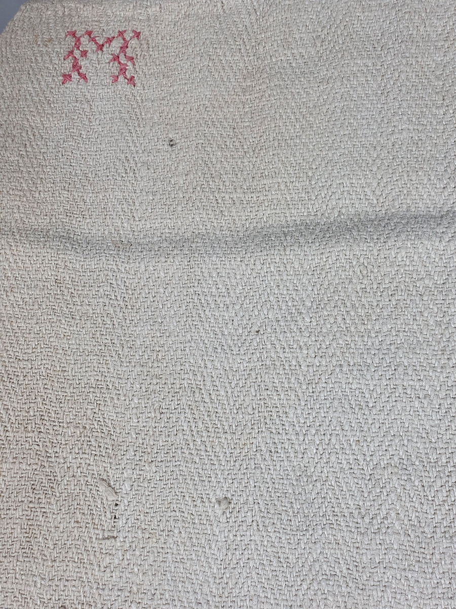 Laken av lin, sydd sammen av to deler, med monogram i det ene hjørnet.