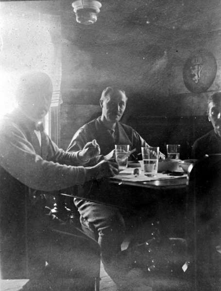 Tre menn ved middagsbord i hytte