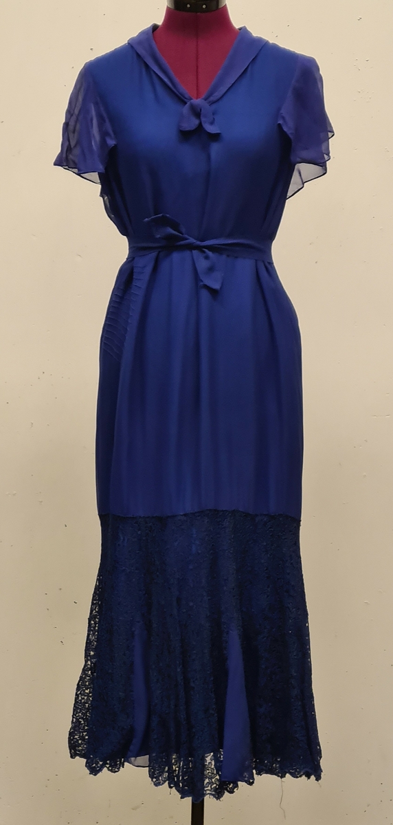 En rak klänning i blått siden. Nedtill på kjolen finns en bred spetsvolang. skärp. Fodrad med ett sidentyg.

Barbro Anderssons mor köpte klänningen på auktion efter handarbetslärarinna i Torskors i Blekinge i början av 1950- talet