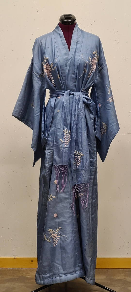 Hela kimonon är broderad i lila och grå toner. Tillhörande knytskärp. Vida ärmar.

Från ca 1926 troligen amerikansk. En moster till givaren Elisabeth Glantzberg som drev Atelje´ Birgitta-skolan i Stockholm verkade även med mode i Amerika.