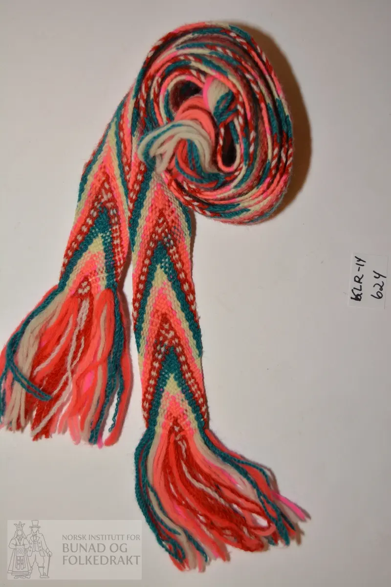 Bånd, Strømpebånd, 2 stk.
Fingra band, i fargene rosa, rødt, hvitt og blågrønt.
Frynser i hver ende.