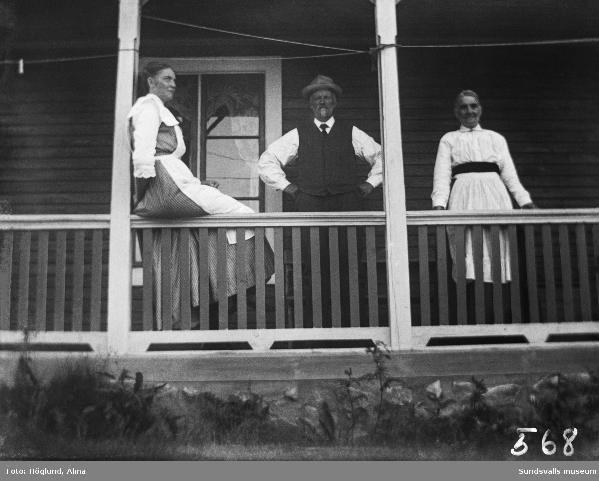 Två kvinnor och en man på verandan till ett hus.