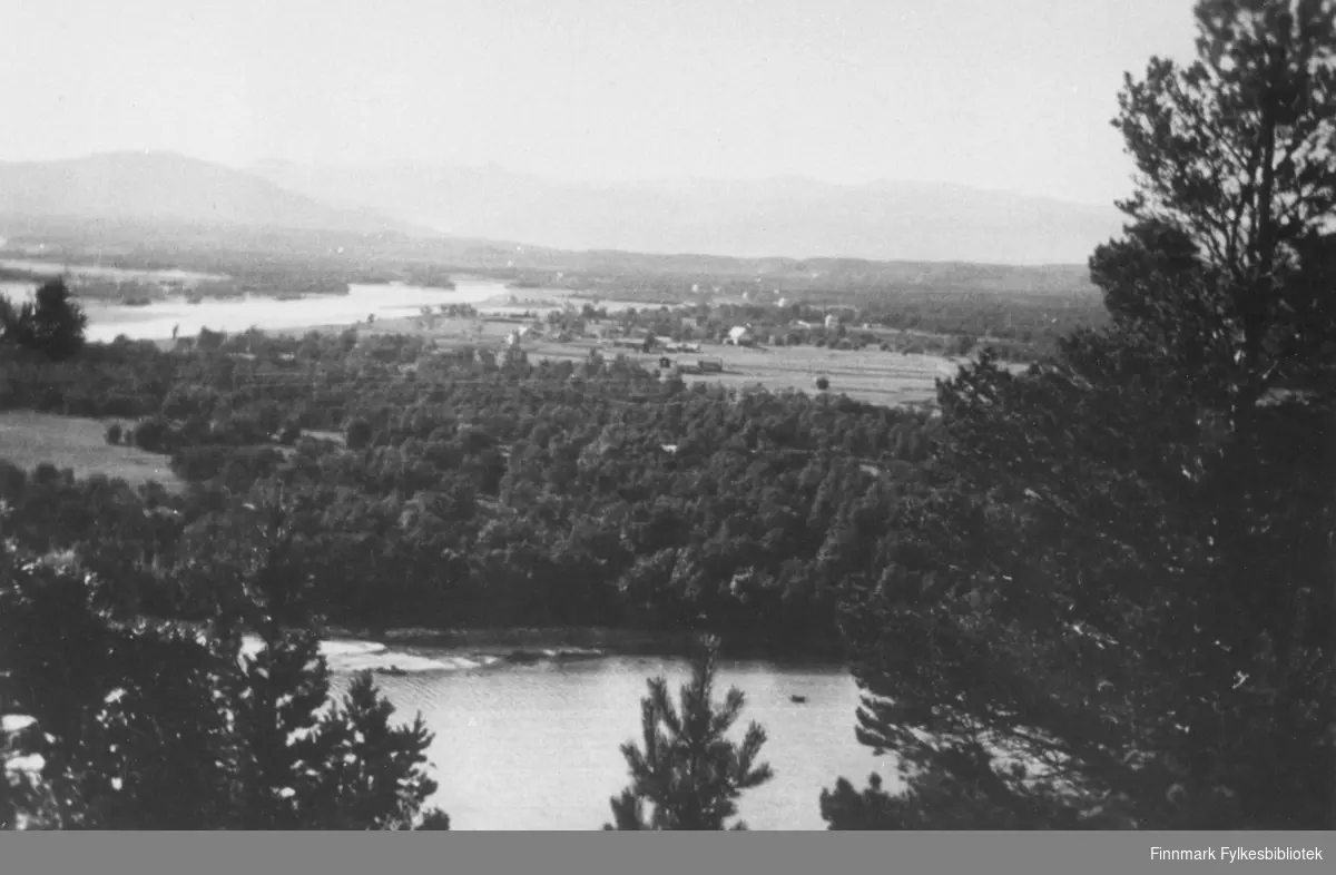 Oversiktsbilde av Elvebakken i Alta. Helt bakerst på bildet ser man bygda. Forran ser man et vann og en skog.