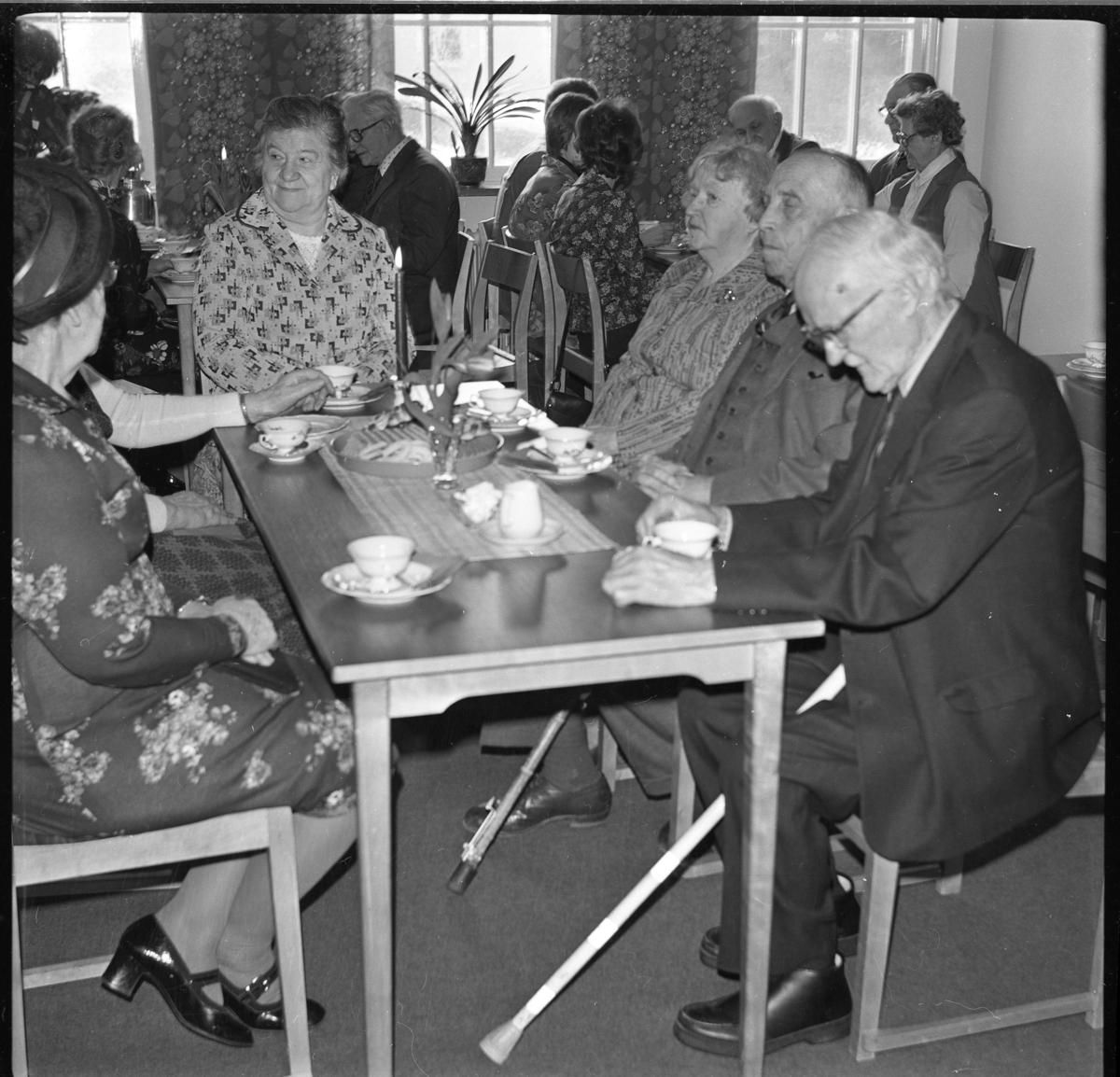 Äldre kvinnor och män sitter vid kaffebord med tända ljus. Det är Filadelfia-församlingen i Gränna som arrangerar "De äldres fest". Vid kortänden sitter Elsa Andersson och snett till höger bakom henne sitter Edvin Johansson.