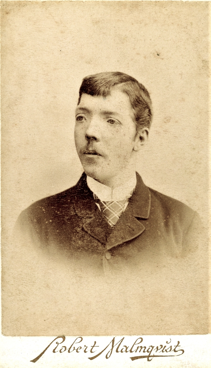 Ateljéporträtt av en okänd ung man med lugg, mustasch och rutig slips. Troligen fotograferad i Halmstad.