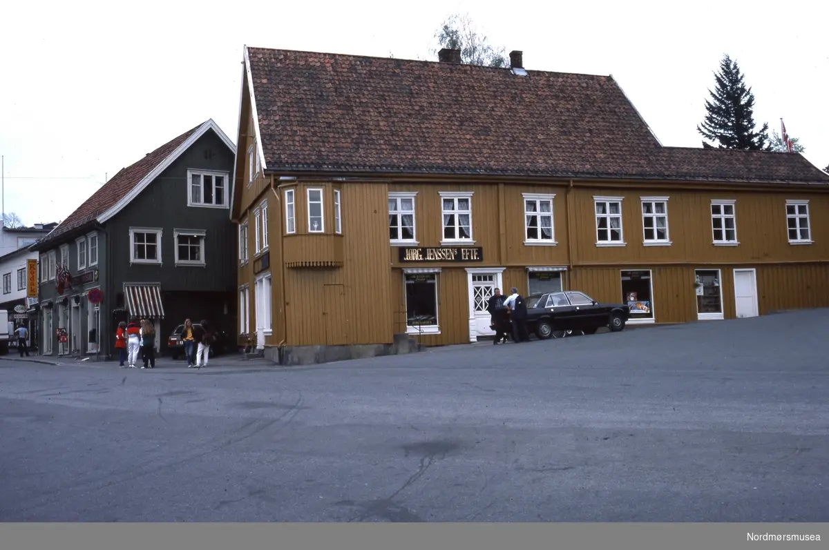 Foto trolig fra et gateparti i Drøbak i Frogn kommune i Viken fylke. Datering er trolig på 1980-tallet. Fra Stein Magne Bach sin private fotosamling. Denne samlingen består av dias fra perioden omkring 1980. Fra Nordmøre museums fotosamlinger.