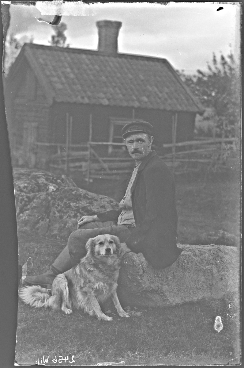 Fotografering beställd av Fredriksson. Man sitter på en sten med sin hund. Han är ej identifierad.